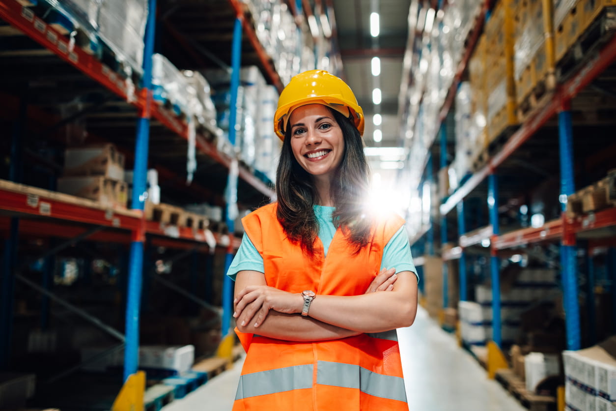 Portrait of a smiling female warehouse worker standing with arms crossed in a large distribution warehouse.